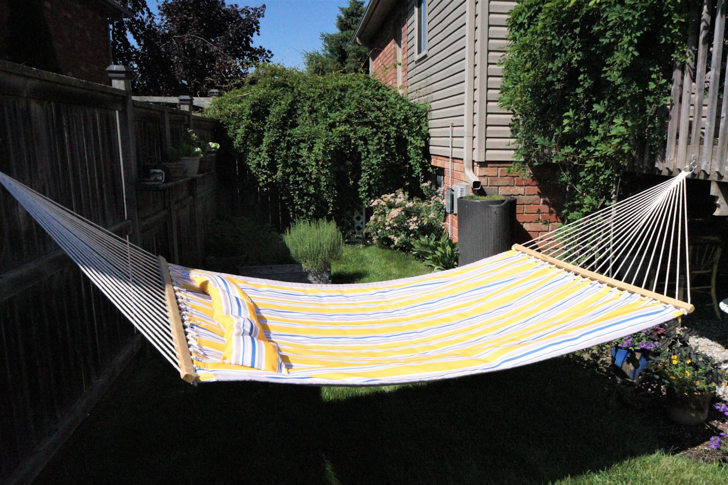 Striped fabric hammock hanging across a residential backyard.