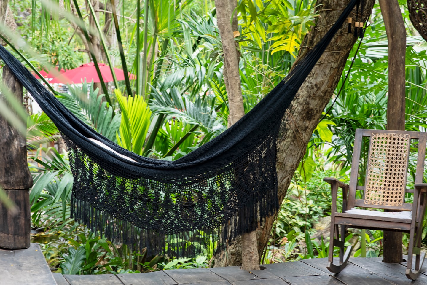 A woven hammock and rocking chair sit on a wooden deck.