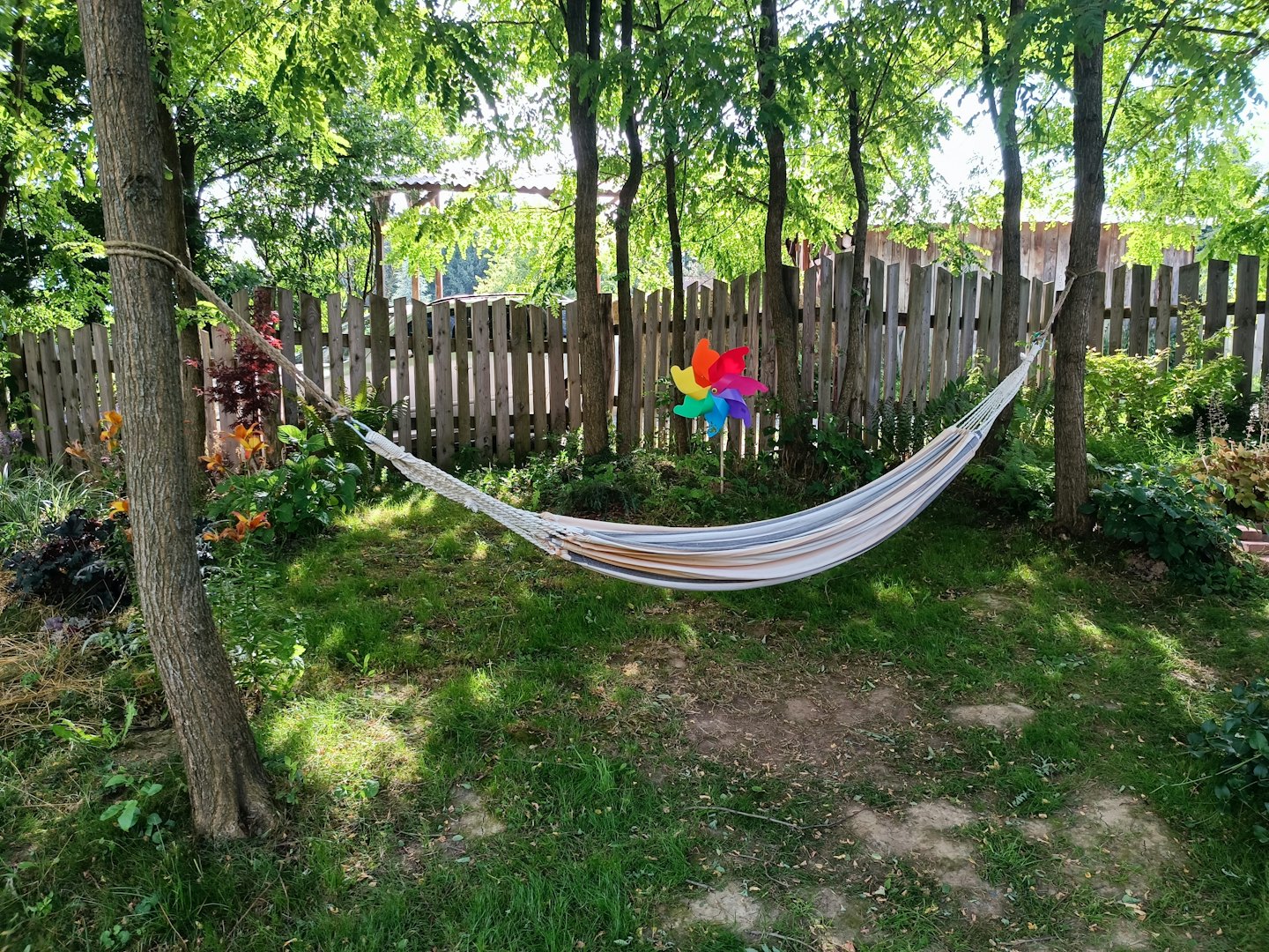 A striped hammock hangs between two trees in a garden.