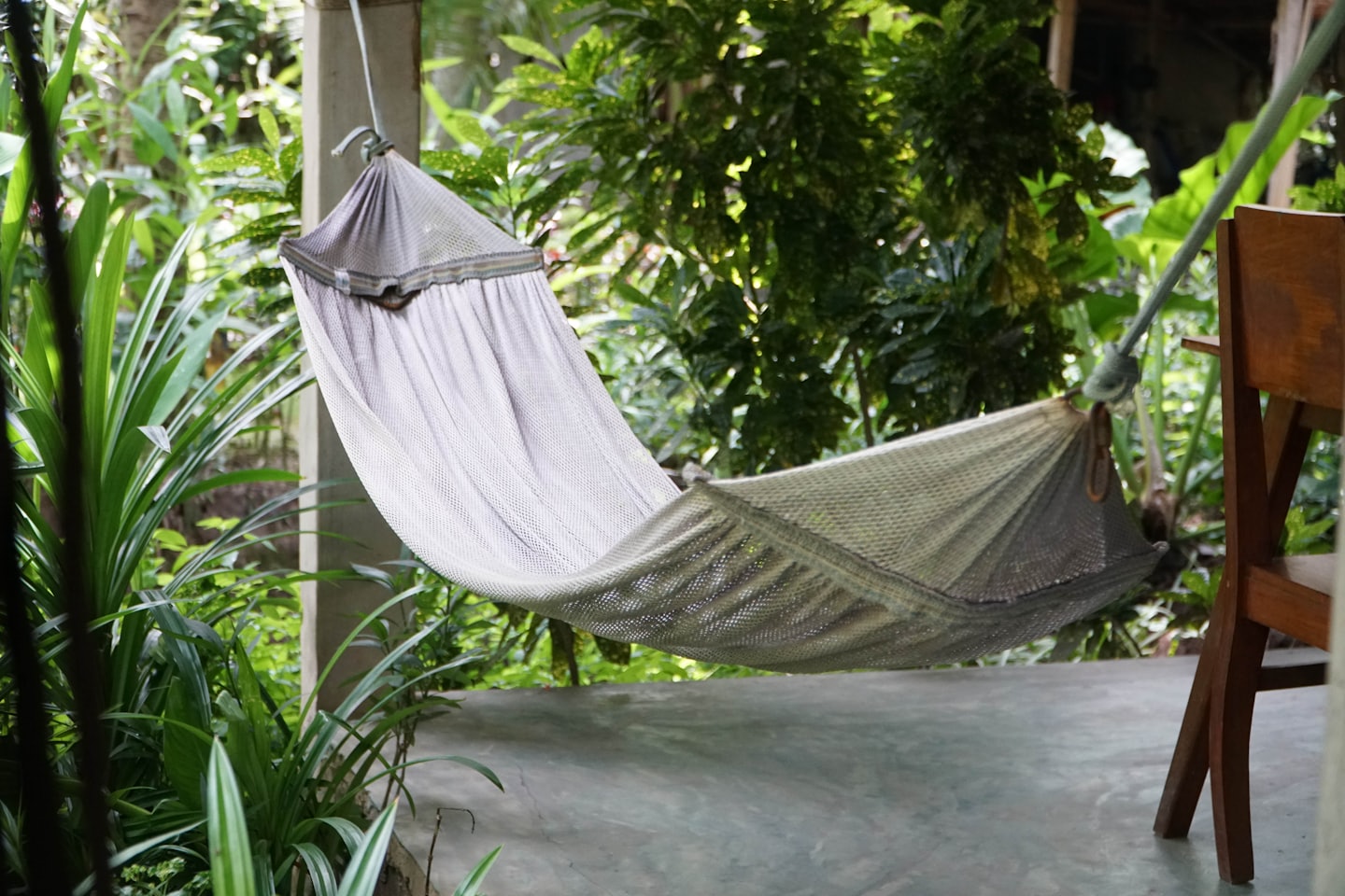 A grey mesh hammock hangs between a pillar and chair.